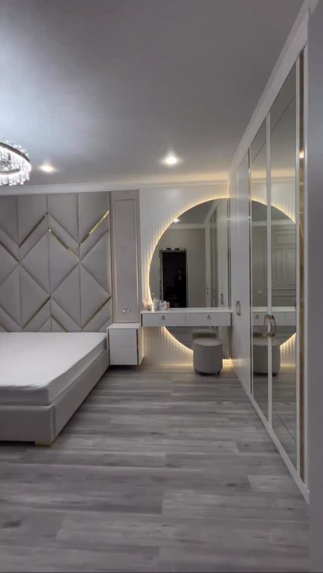Luxury bedroom with geometric padded headboard, circular backlit mirror, and mirrored wardrobes.