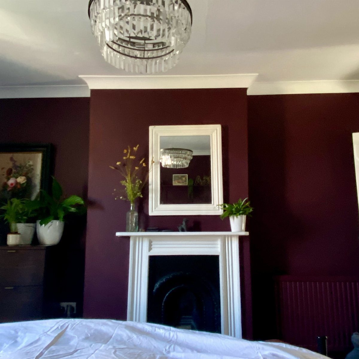 Deep plum purple bedroom walls with a white fireplace and crystal chandelier.