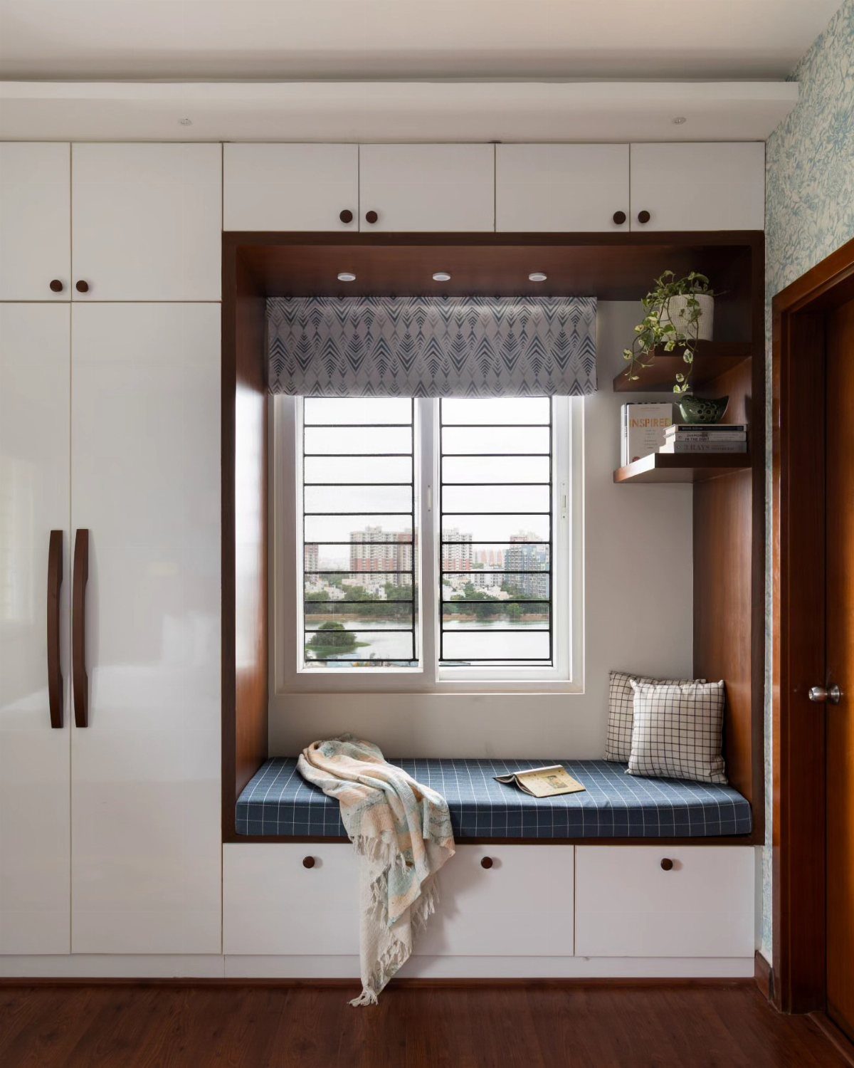 Built-in window nook with blue cushion and white wardrobes in a modern bedroom.