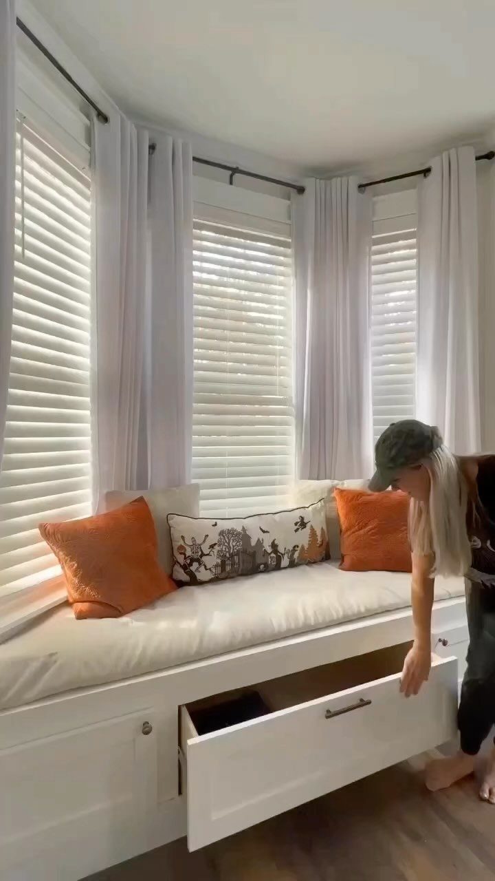 Built-in white window seat with storage drawer being opened in a bright bedroom