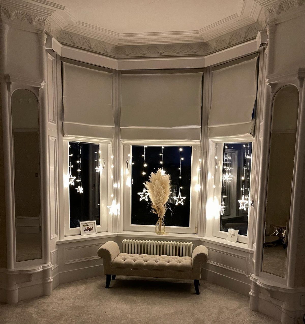 Bay window with star fairy lights and a beige tufted settee in a bedroom