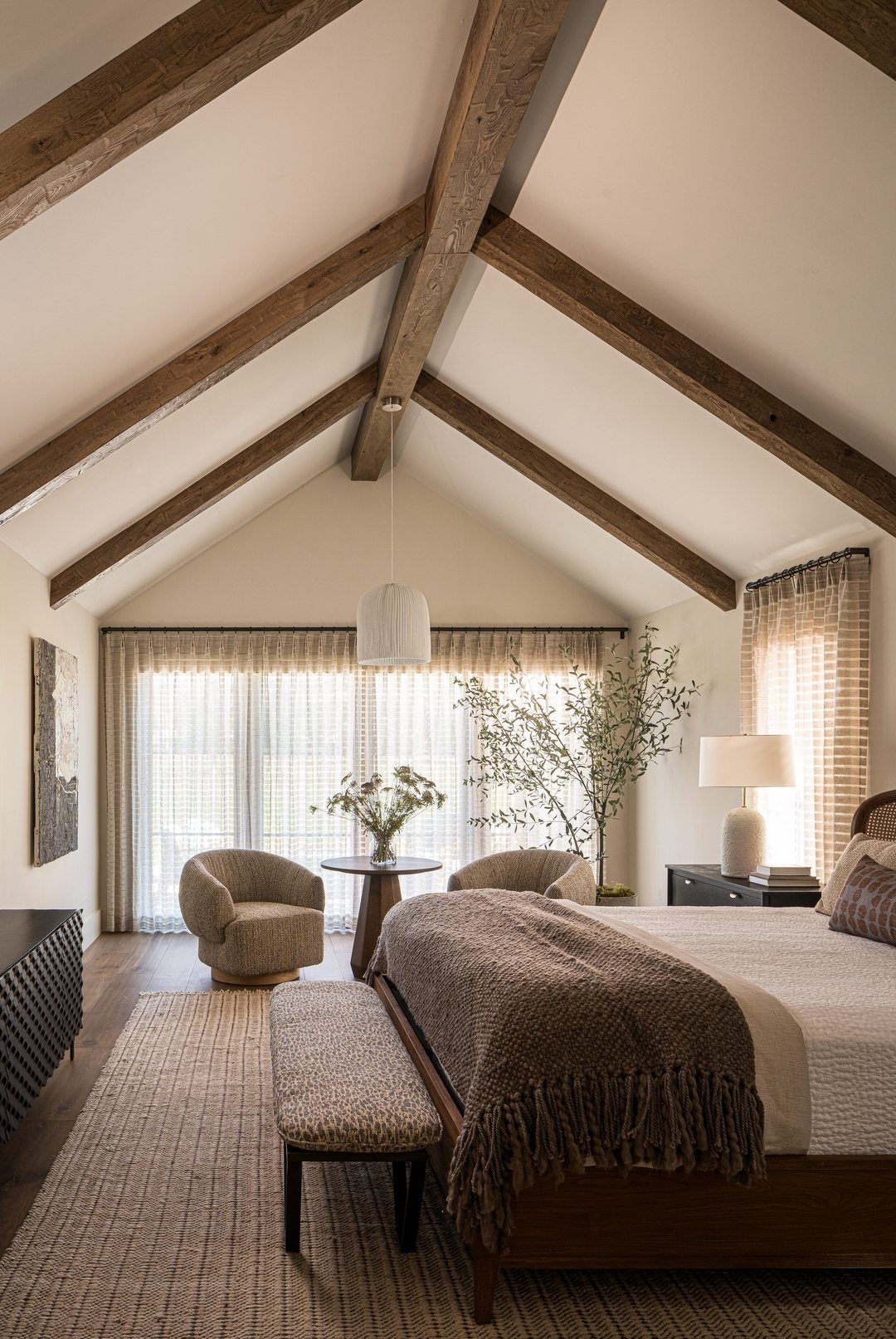 Vaulted bedroom ceiling with dark brown exposed wooden beams and neutral decor.