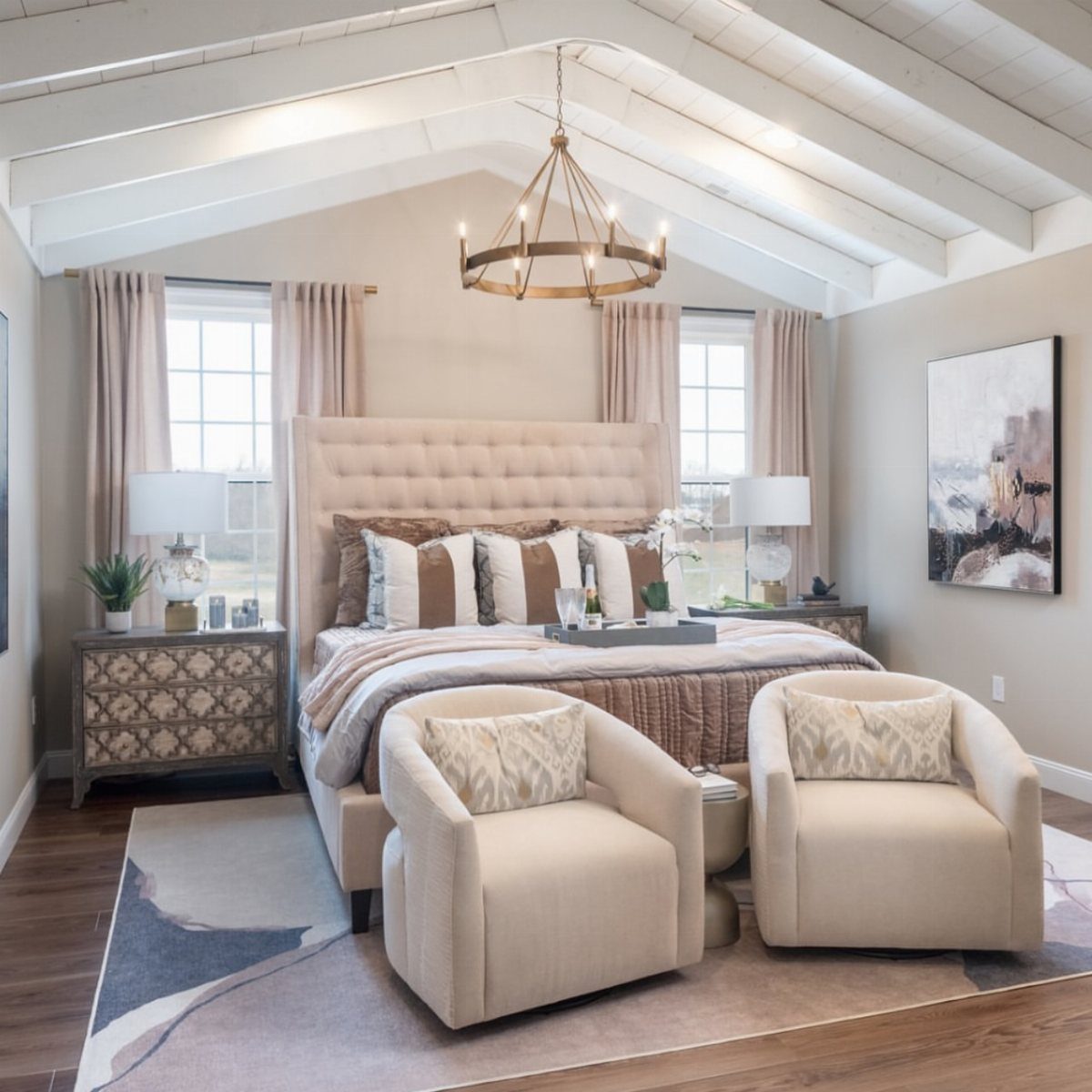 Bedroom with white cathedral ceiling, tufted headboard, and two beige armchairs.