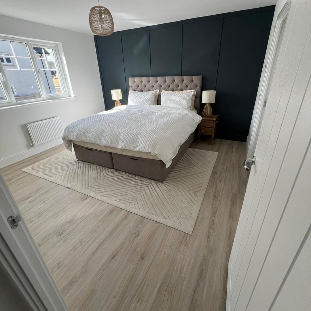 Light wooden flooring in a bedroom with a white bed and navy wall.
