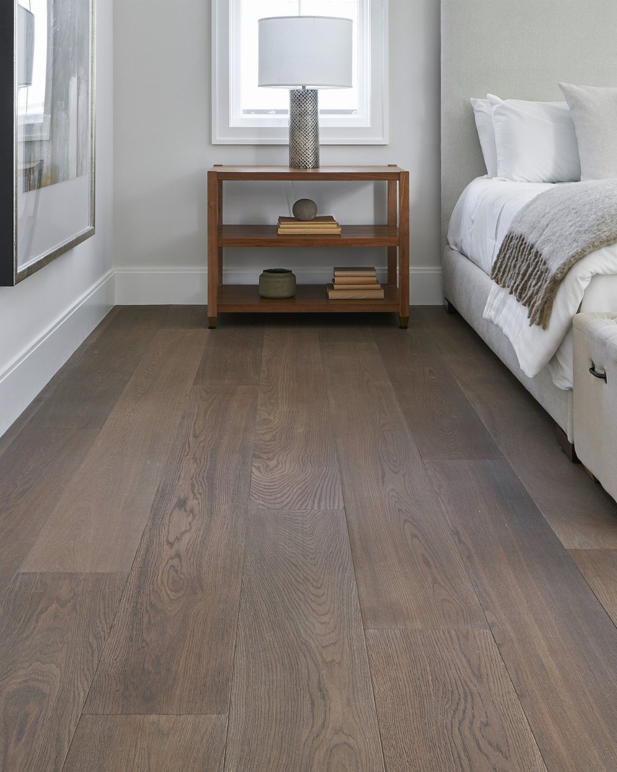 Brown wooden plank flooring in a bedroom with a white bed and nightstand.