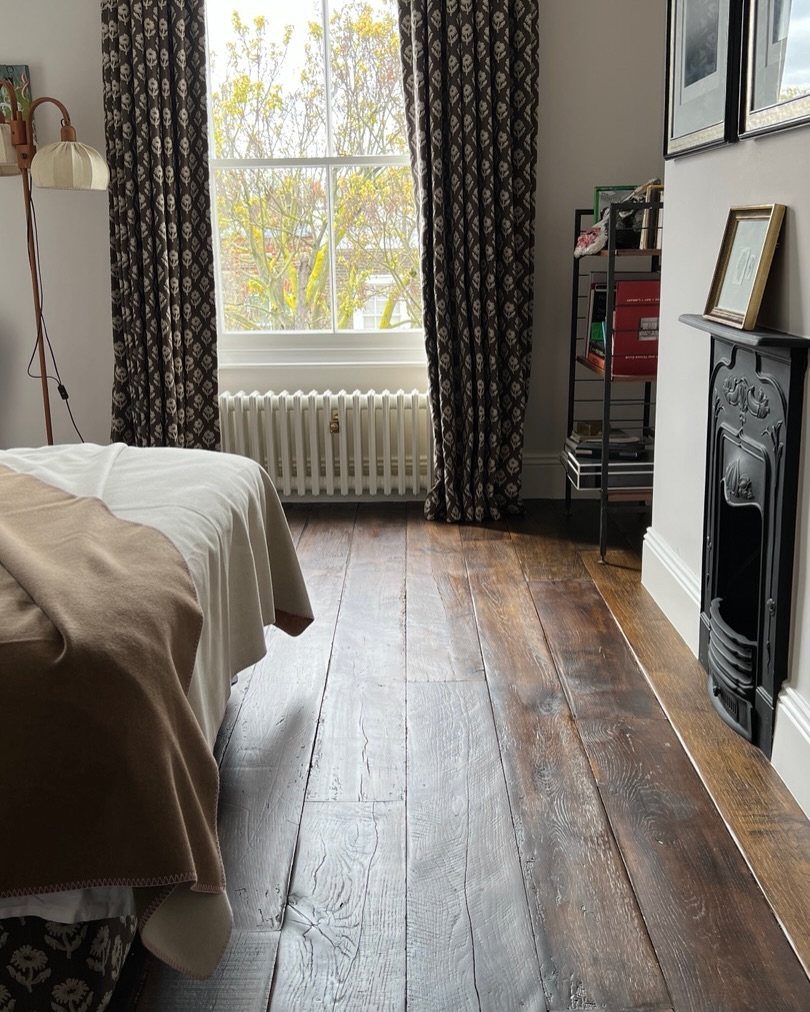 Rustic reclaimed wood flooring in a bedroom with a black fireplace and window.
