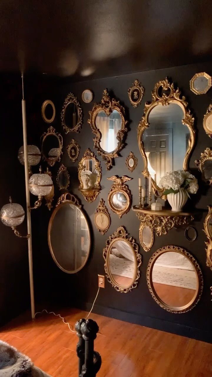 Ornate gold mirrors arranged on a matte black accent wall with wood floors.