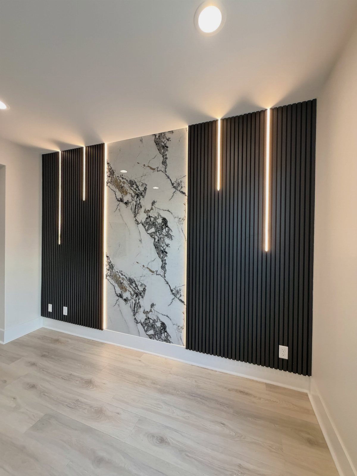 Black slatted wall panels with a central marble slab and integrated vertical lighting.