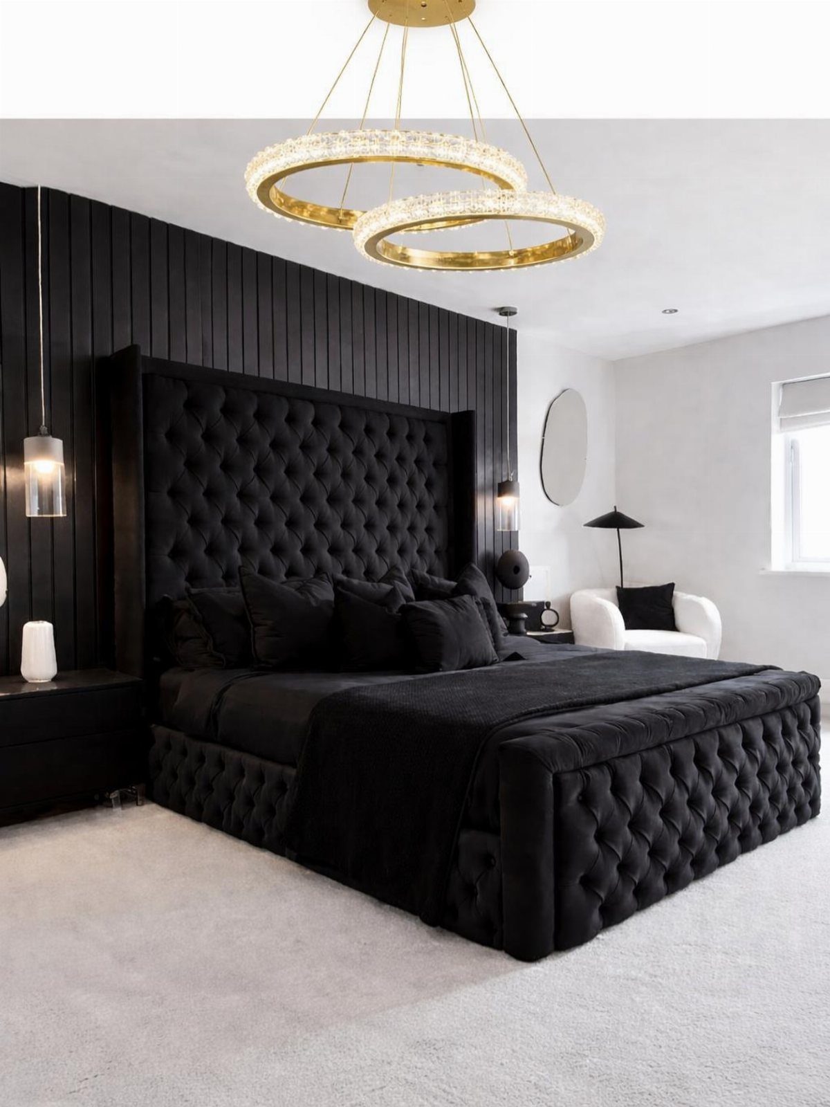 Black tufted bed in a bedroom with black walls and grey carpeting.