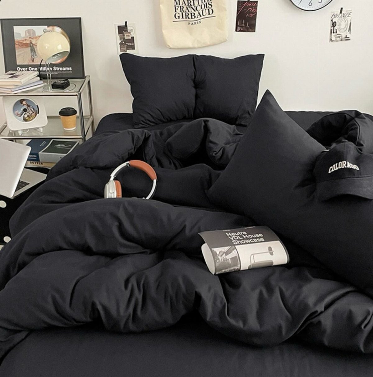 Black bedding and pillows on a bed against a white wall with decor.
