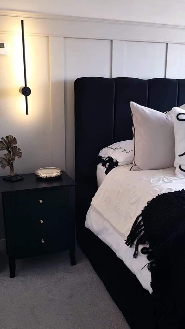 Black velvet headboard and nightstand against light grey paneled walls with white bedding.