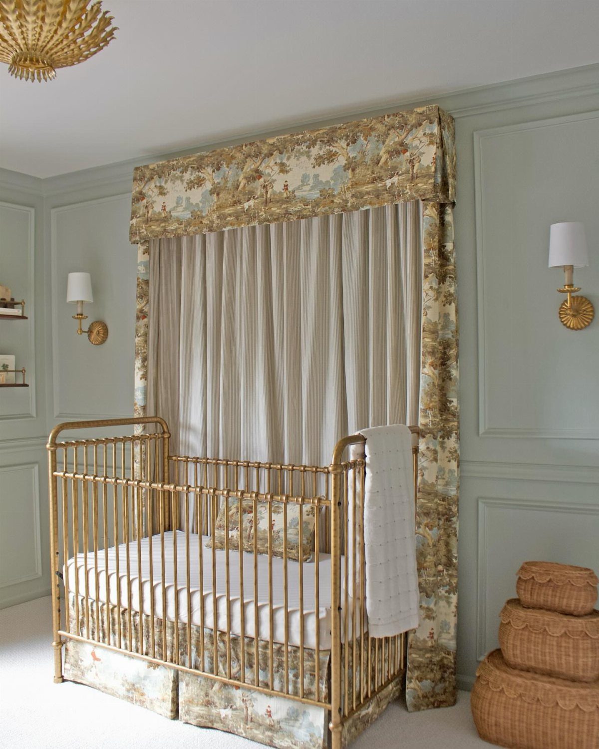 Gold metal crib in a pale green nursery with layered patterned curtains