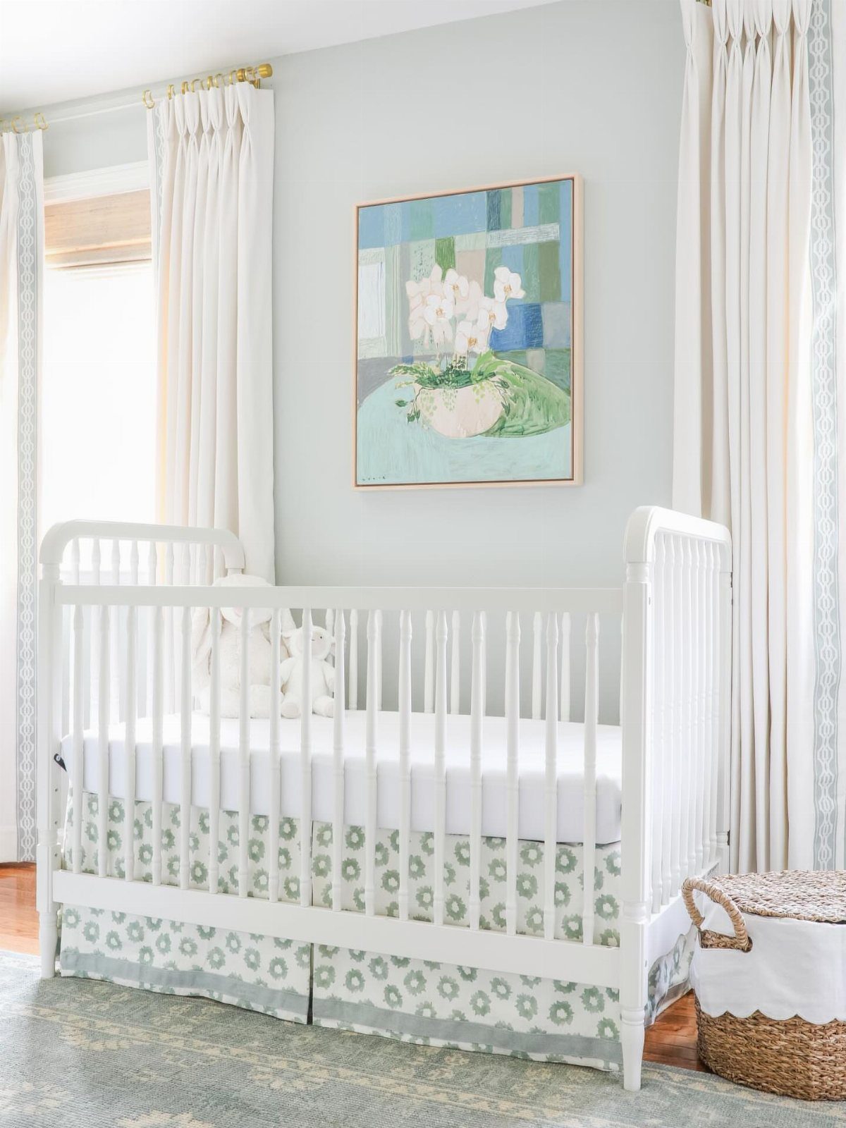 White crib with green patterned bedding in a light blue nursery room