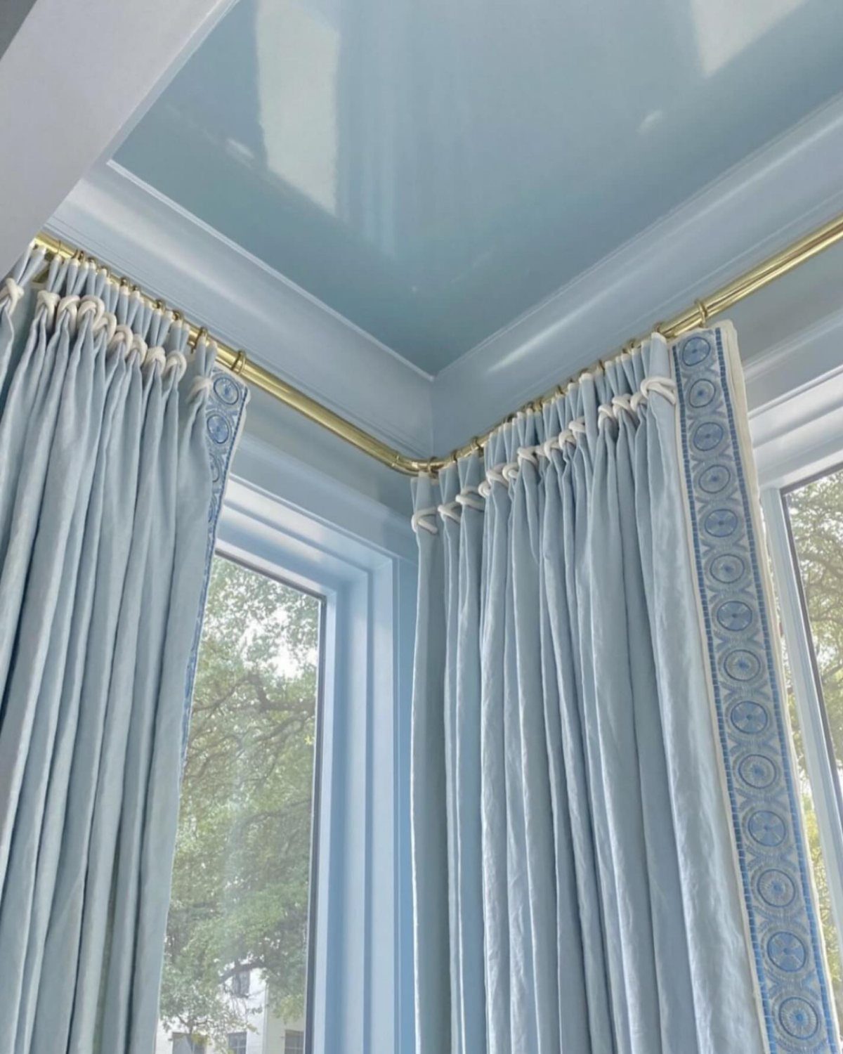Light blue curtains with gold rods under a glossy light blue ceiling.