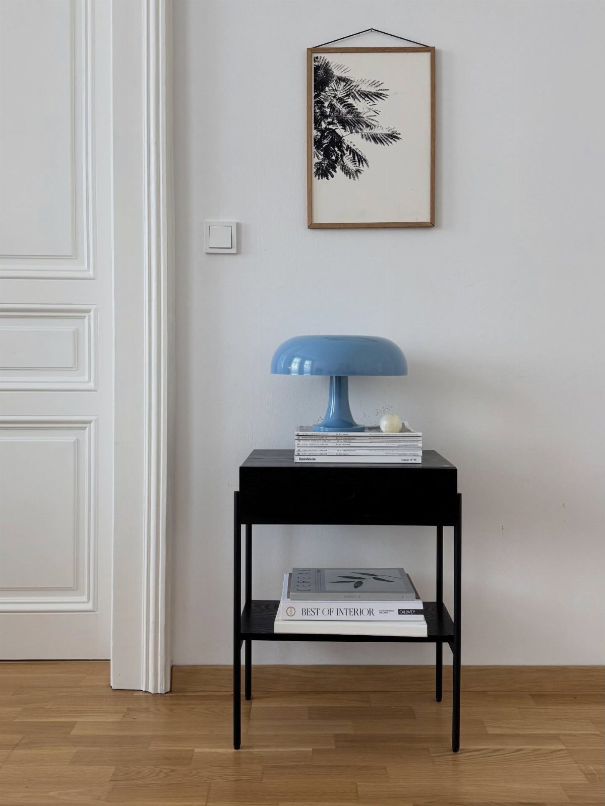 Light blue mushroom lamp on a black side table against a white wall
