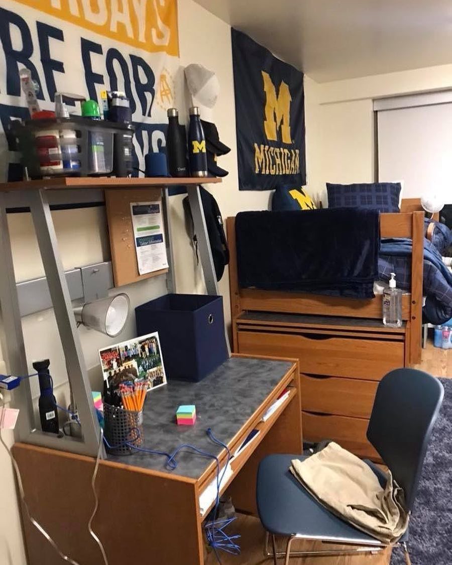 College dorm room with blue bedding, blue storage, and Michigan university banners.