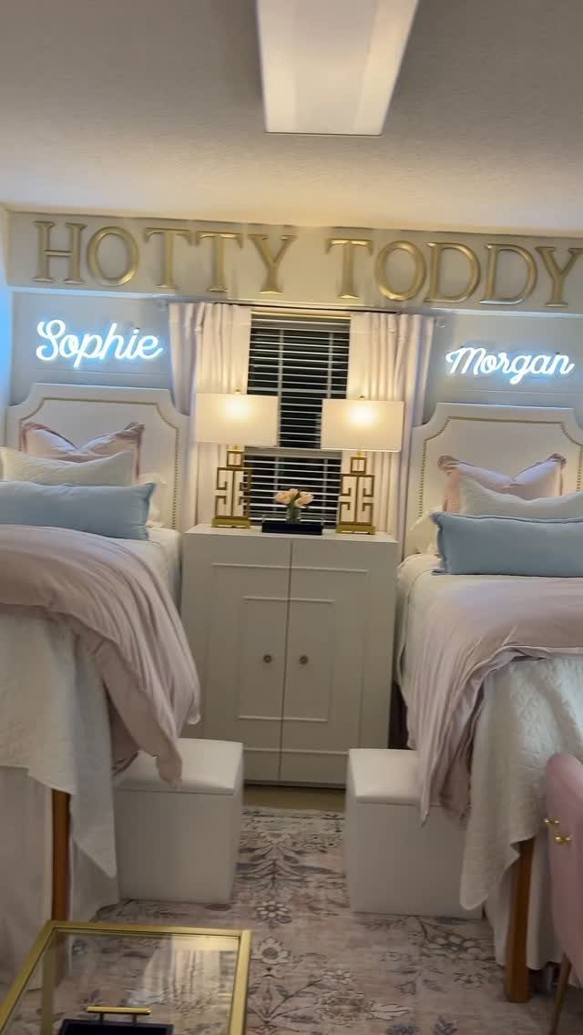Two gold lamps on a white cabinet between two beds in a dorm.