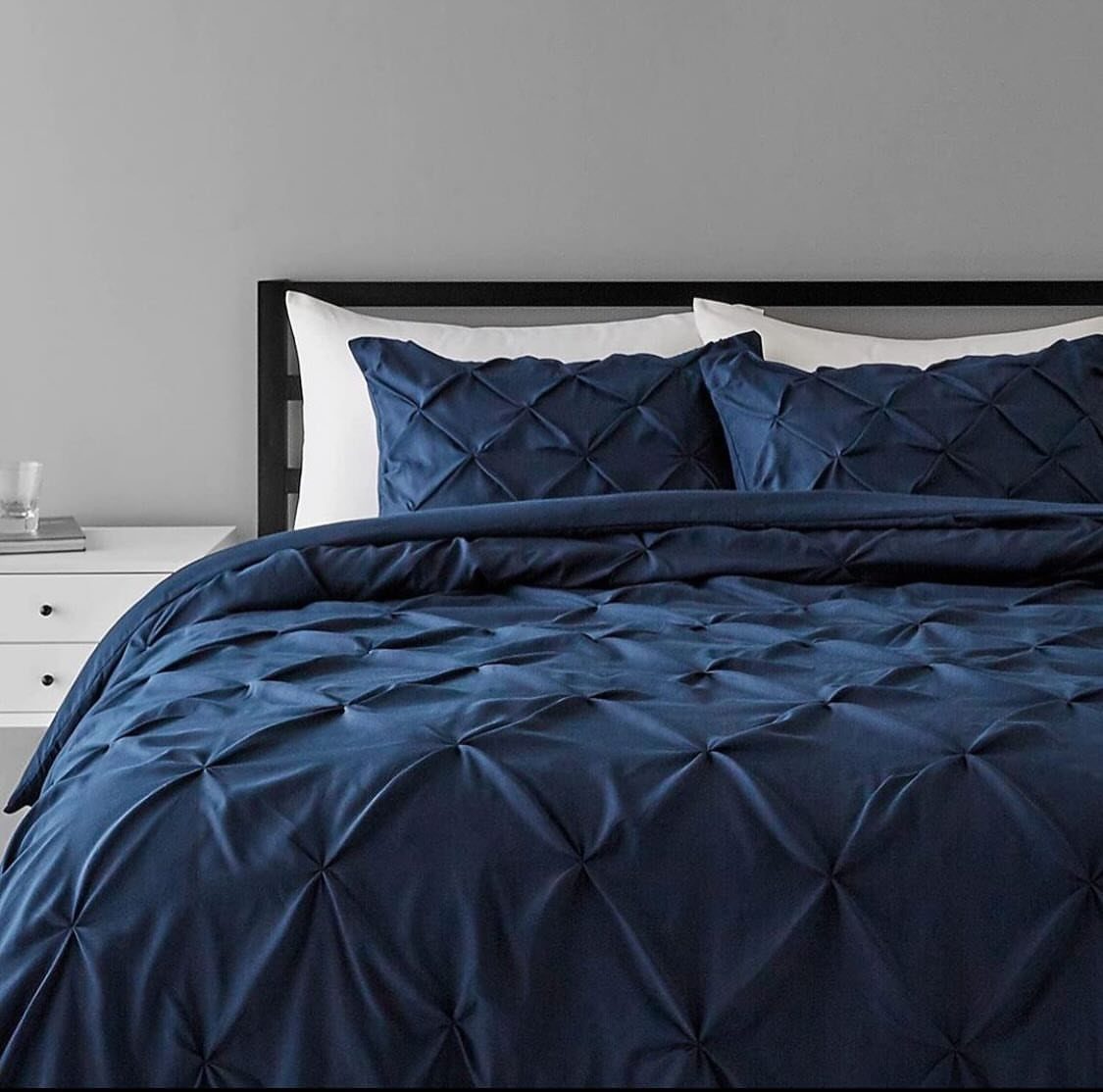 Navy blue pintuck comforter and pillows on a bed with white accents.