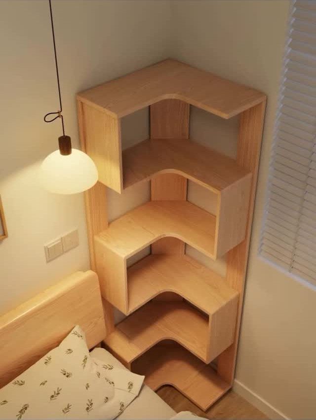 Light wood corner bookshelf standing next to a bed in a bedroom.