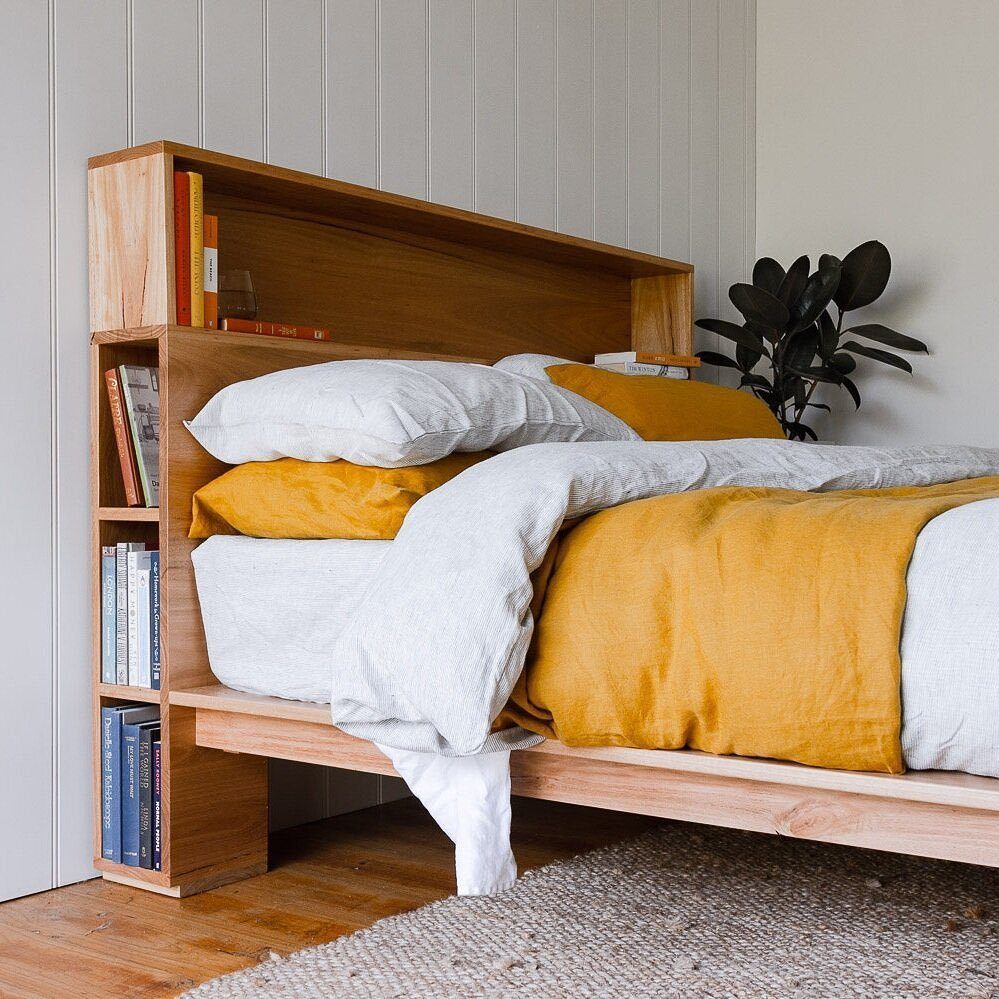 Wooden bed frame with a built-in headboard bookshelf holding several books.
