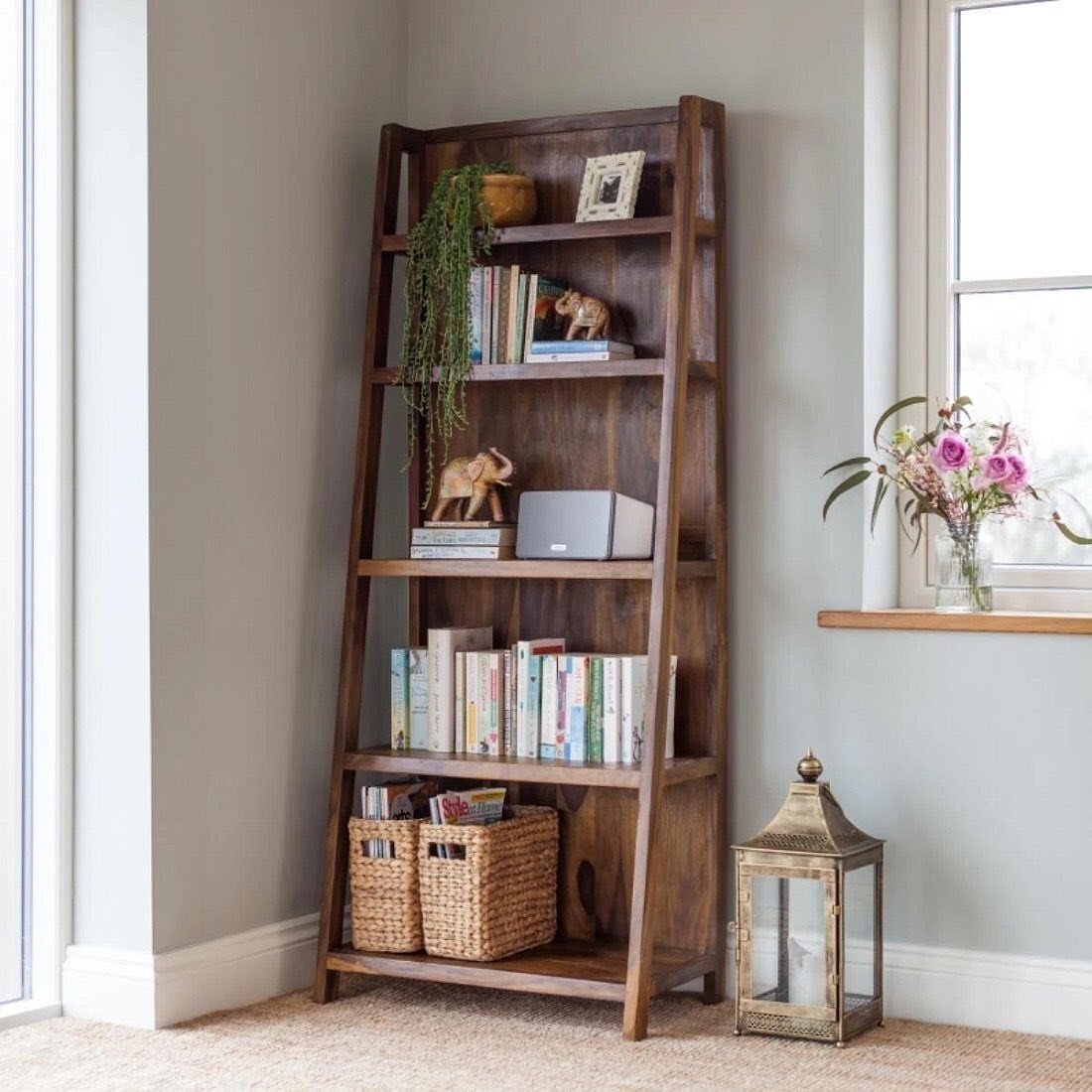 Dark brown wooden ladder bookshelf with books and baskets against a grey wall