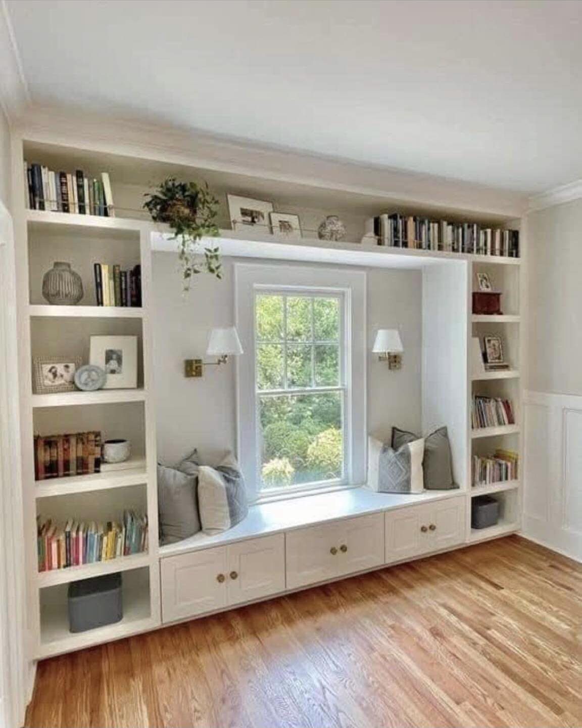 White built-in bookcases surrounding a window seat with cushions and storage drawers.