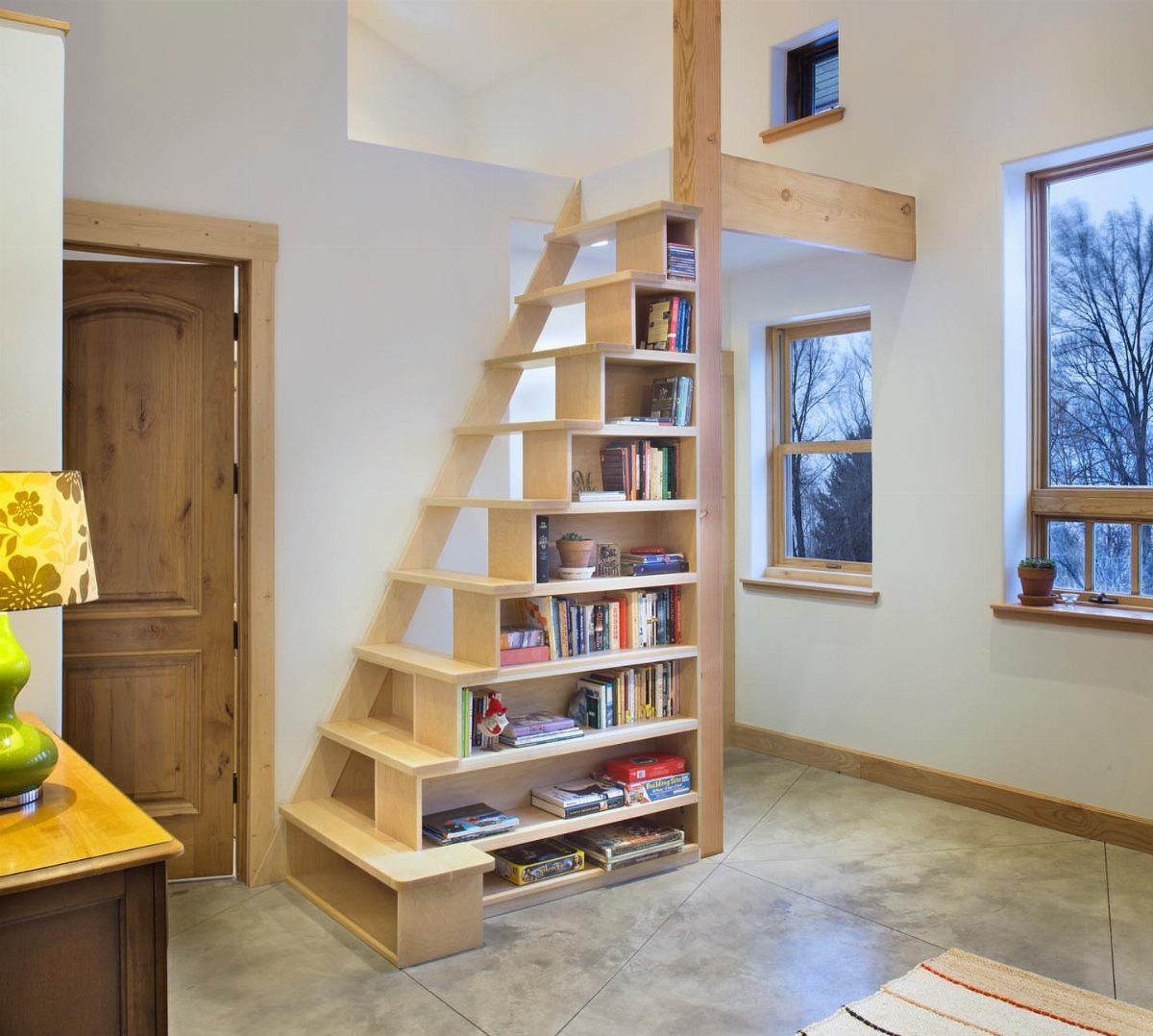 Wooden staircase with built-in bookshelves leading to a loft in a bright room.