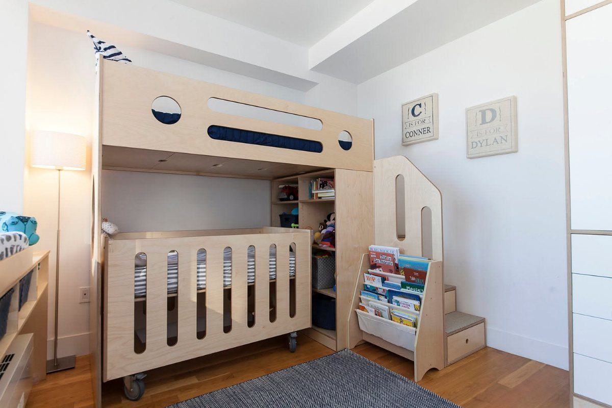 Custom light wood bunk bed with a mobile crib underneath and integrated bookshelves.