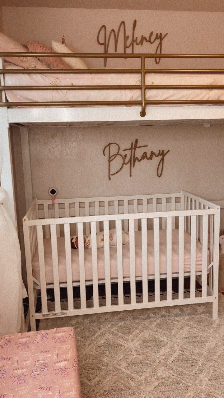 White loft bed with a white wooden crib placed underneath in a pink room.