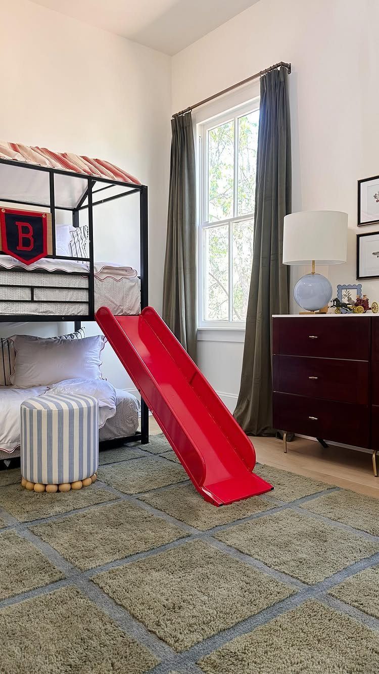Bunk bed with a red slide, striped roof, and grey textured rug.