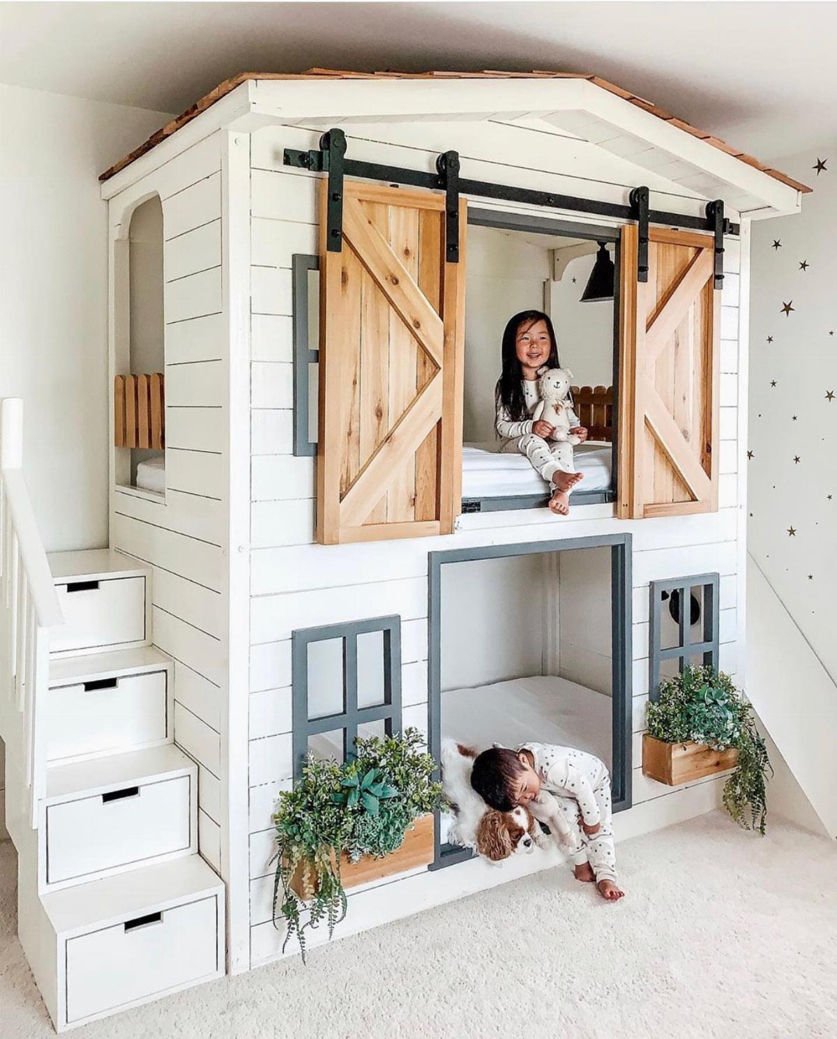 House-shaped white bunk bed with barn doors and children playing inside.