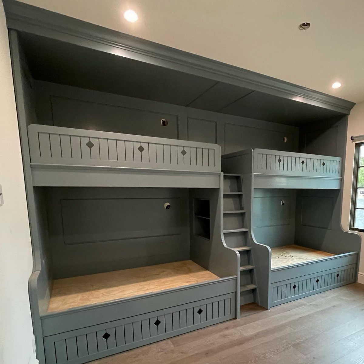 Grey built-in bunk beds with wooden bases and storage drawers in a bedroom.