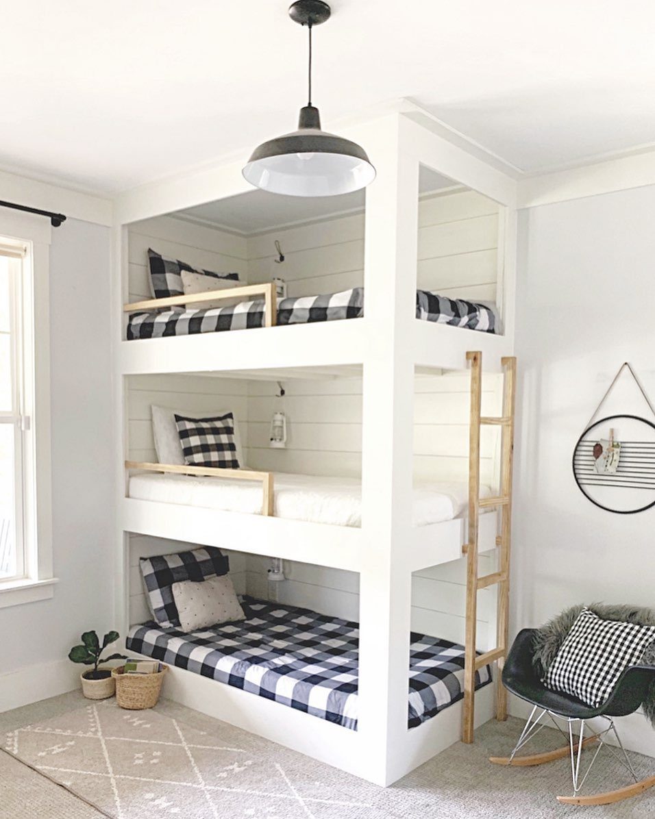 White built-in triple bunk beds with black and white checkered bedding and wooden ladder.