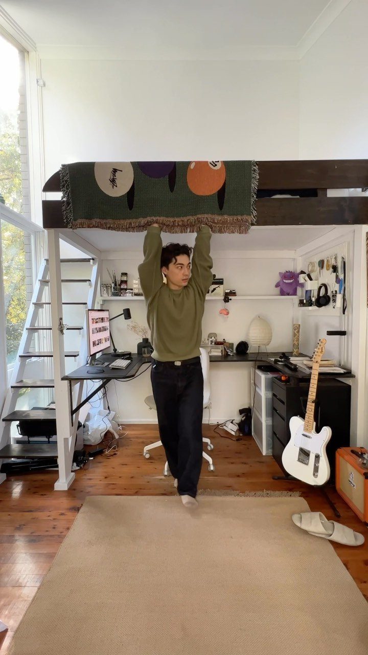 Person standing under a loft bed with a desk and electric guitar below.