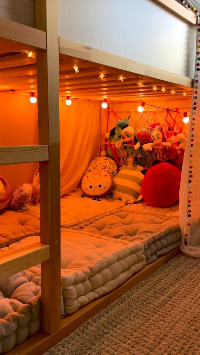 Cozy reading nook under a bunk bed with plush toys and warm string lights.