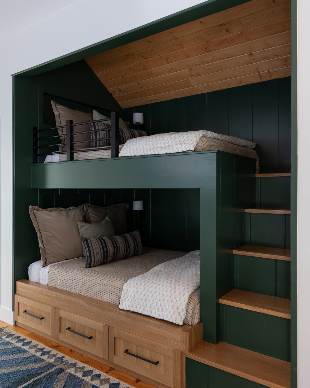 Dark green built-in bunk beds in a recessed alcove with wooden stairs.