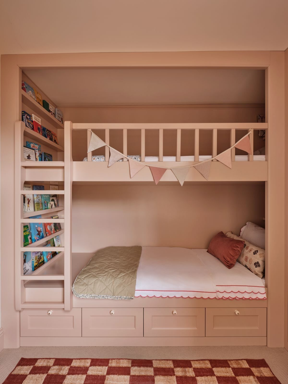 Built-in pink bunk beds recessed into a wall niche with integrated bookshelves.