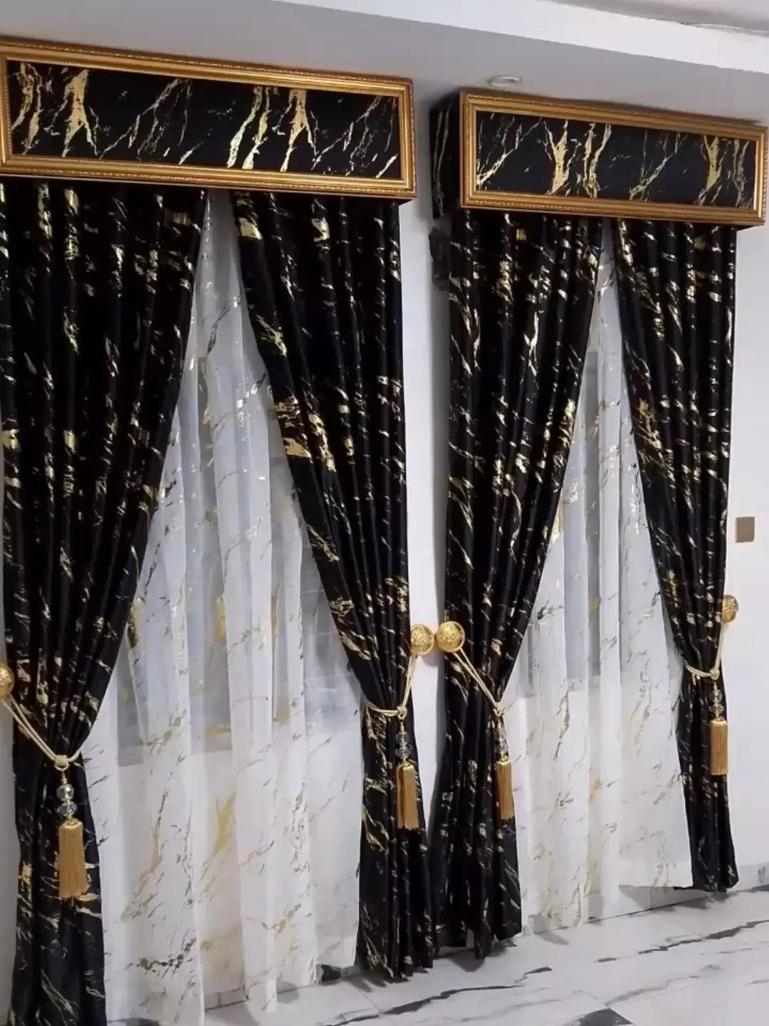 Black and gold marble patterned curtains with sheer white under-curtains and gold tassels.