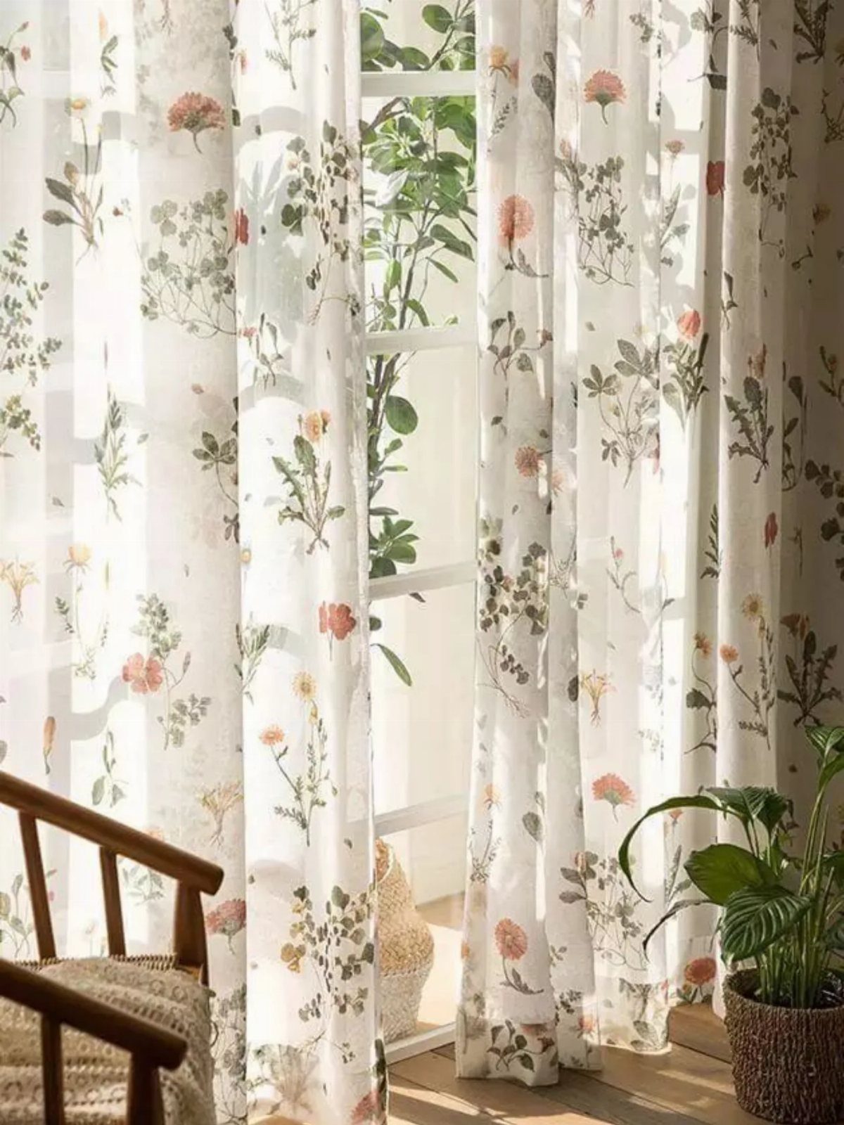 White sheer curtains with orange floral patterns hanging by a sunny window.