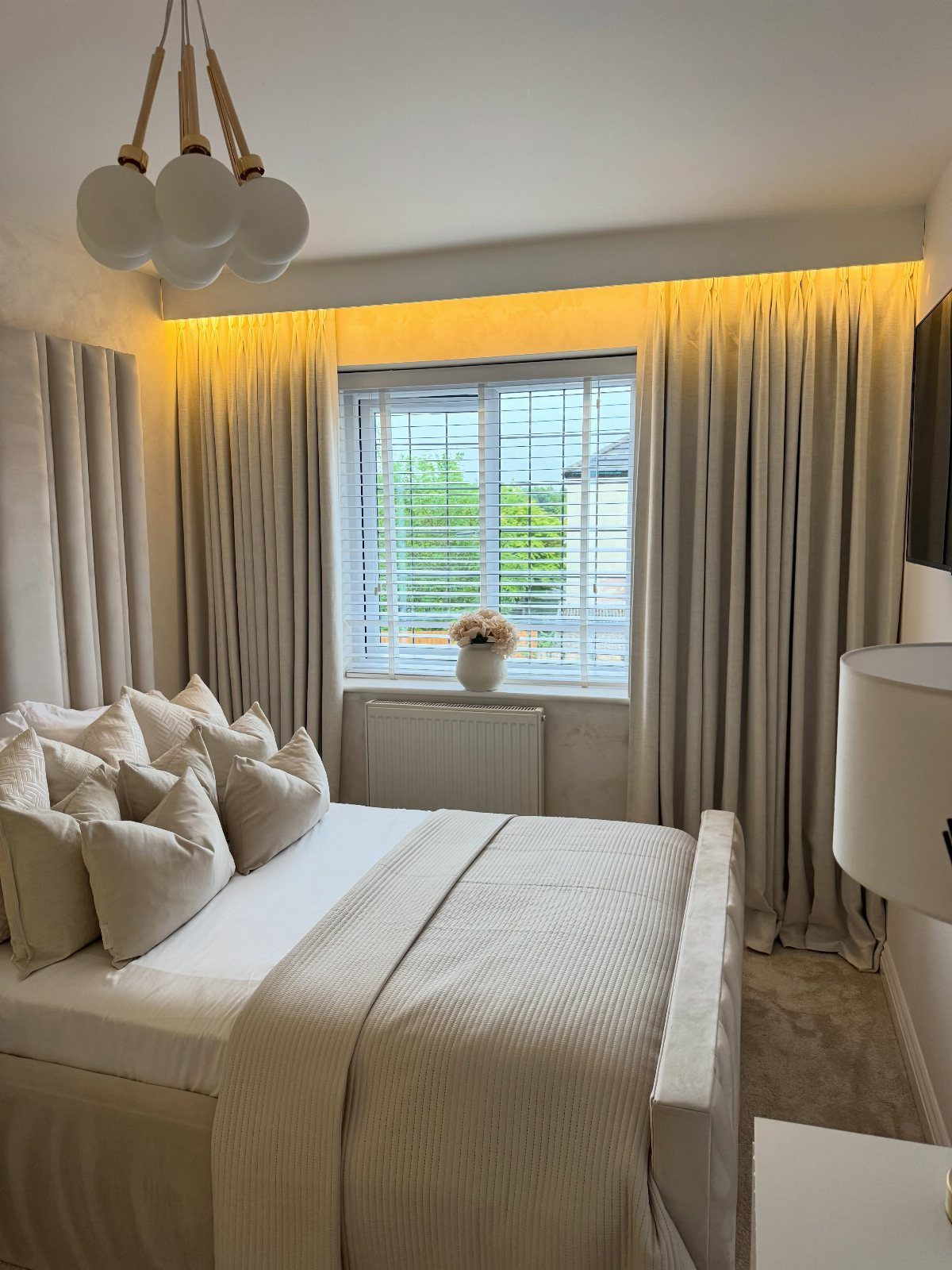 Beige curtains hung from the ceiling in a neutral toned bedroom with a bed.