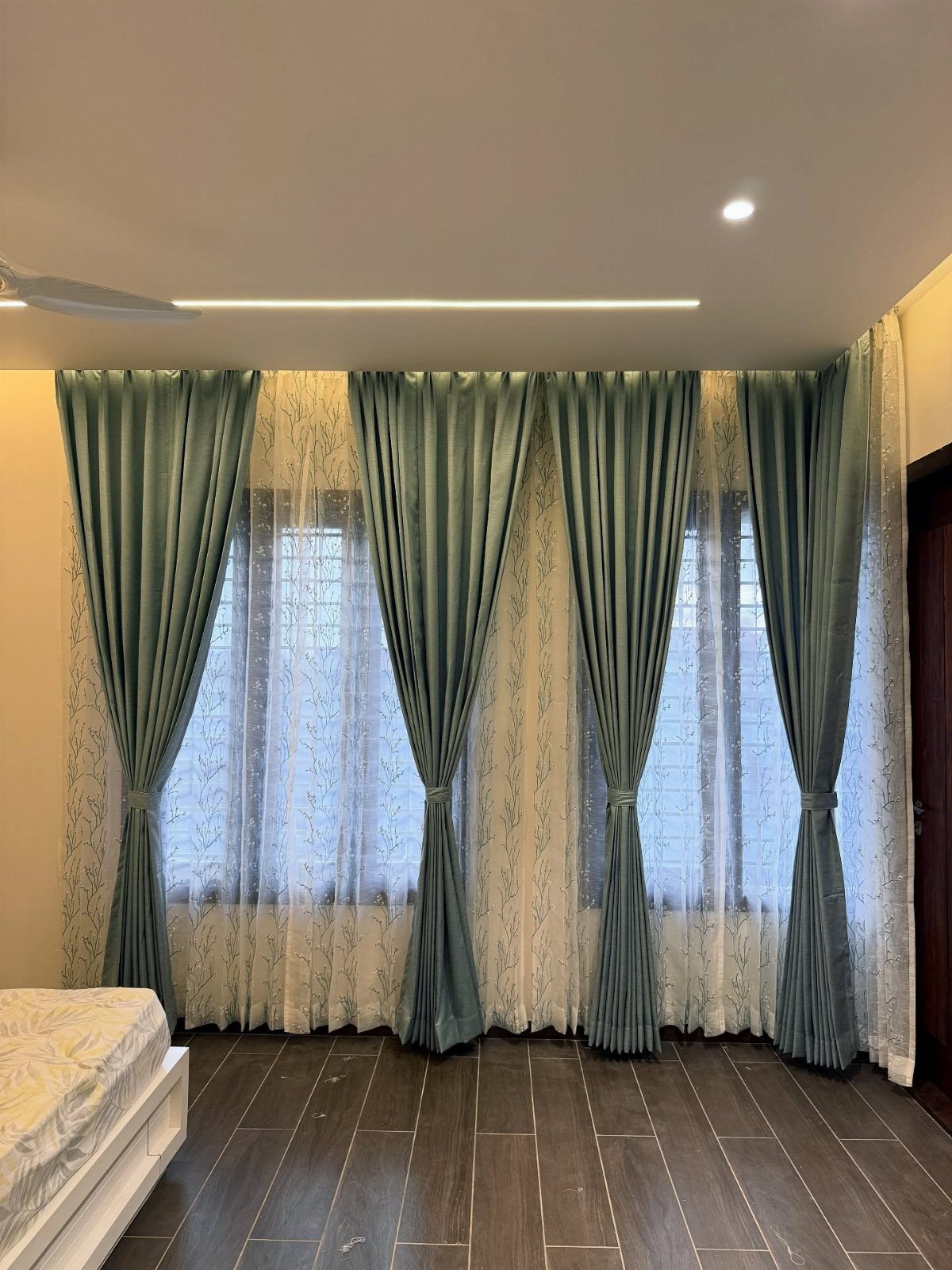 Layered curtains with sheer white lace and tied-back teal fabric in a bedroom.