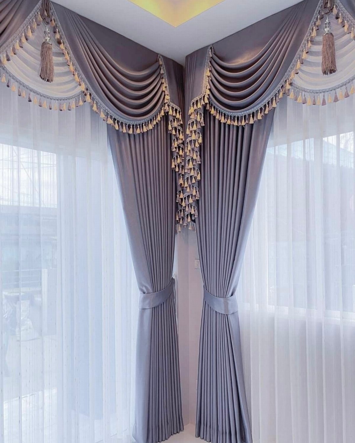 Grey satin curtains with gold tassel valances and sheer white under-curtains.