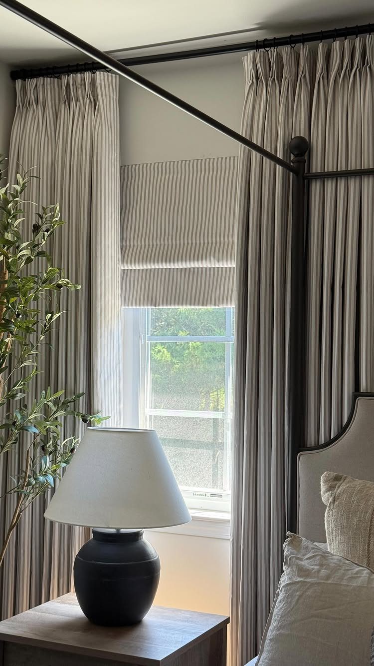 Vertical striped grey and white curtains and Roman shade in a bedroom setting.