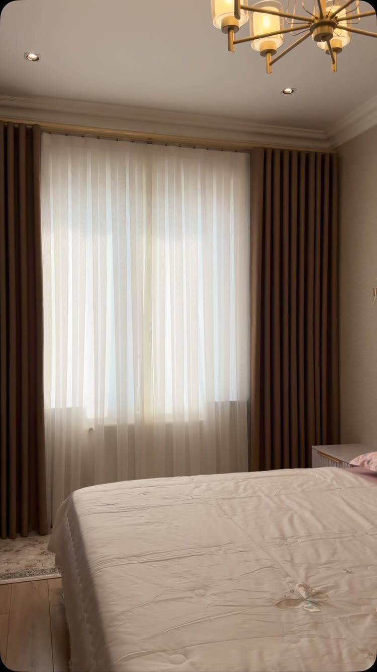 Brown solid curtains and sheer white curtains framing a bedroom window