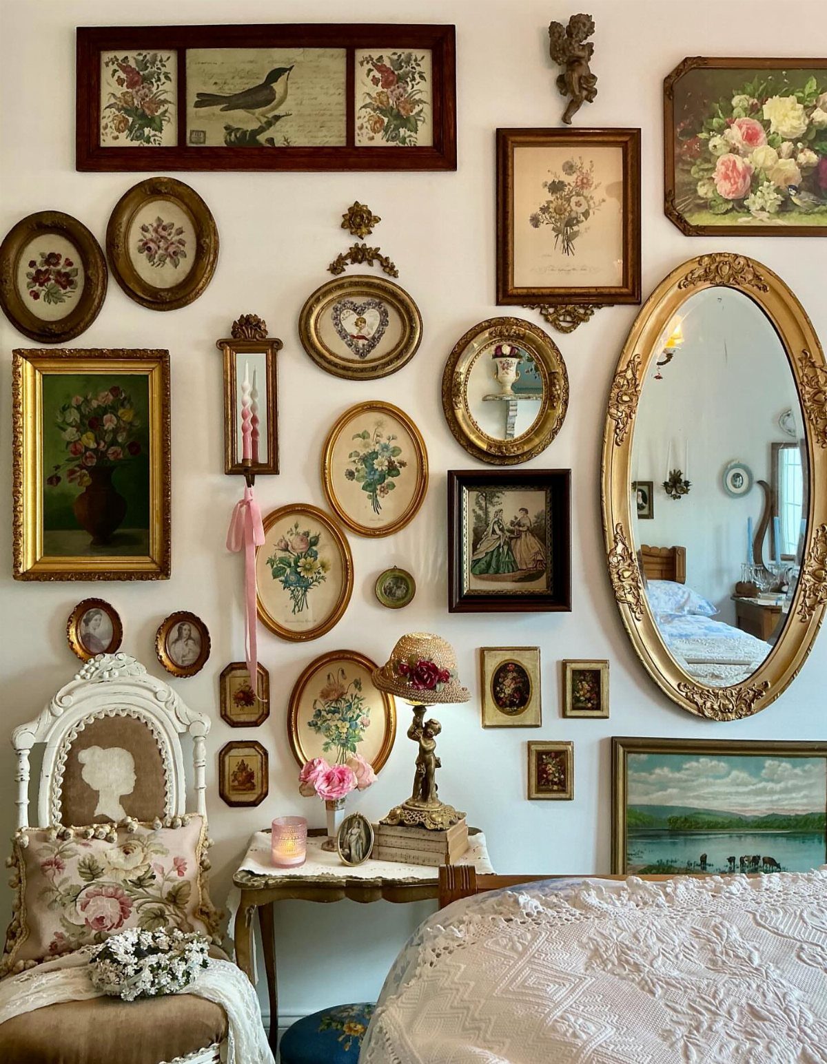 Gallery wall with multiple gold-framed paintings and a mirror above a bed.
