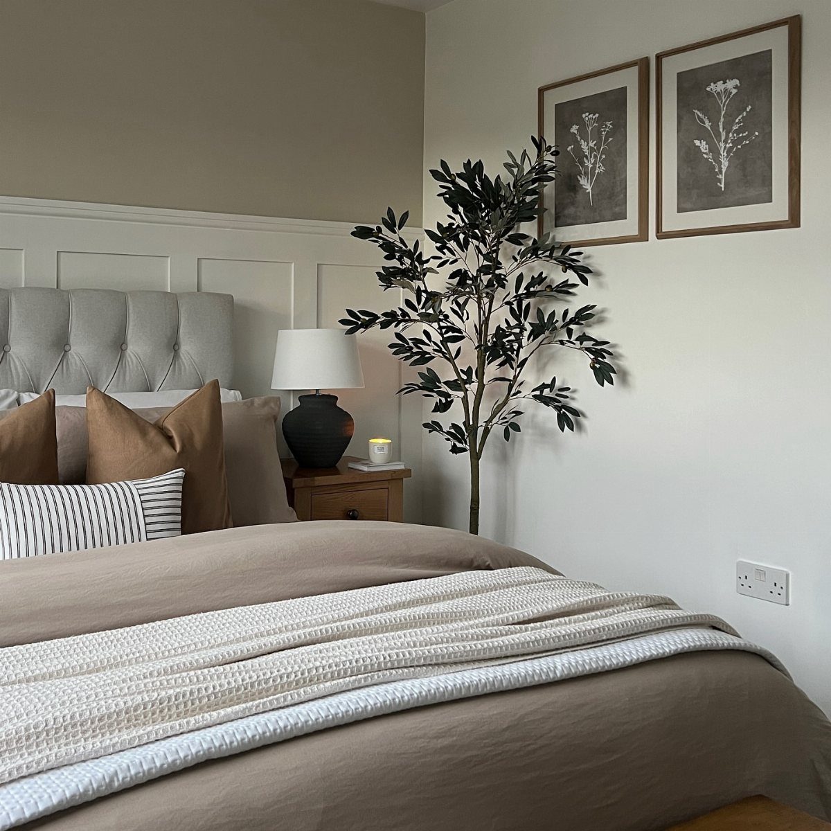 Two framed botanical prints hanging on a white wall above a bed.