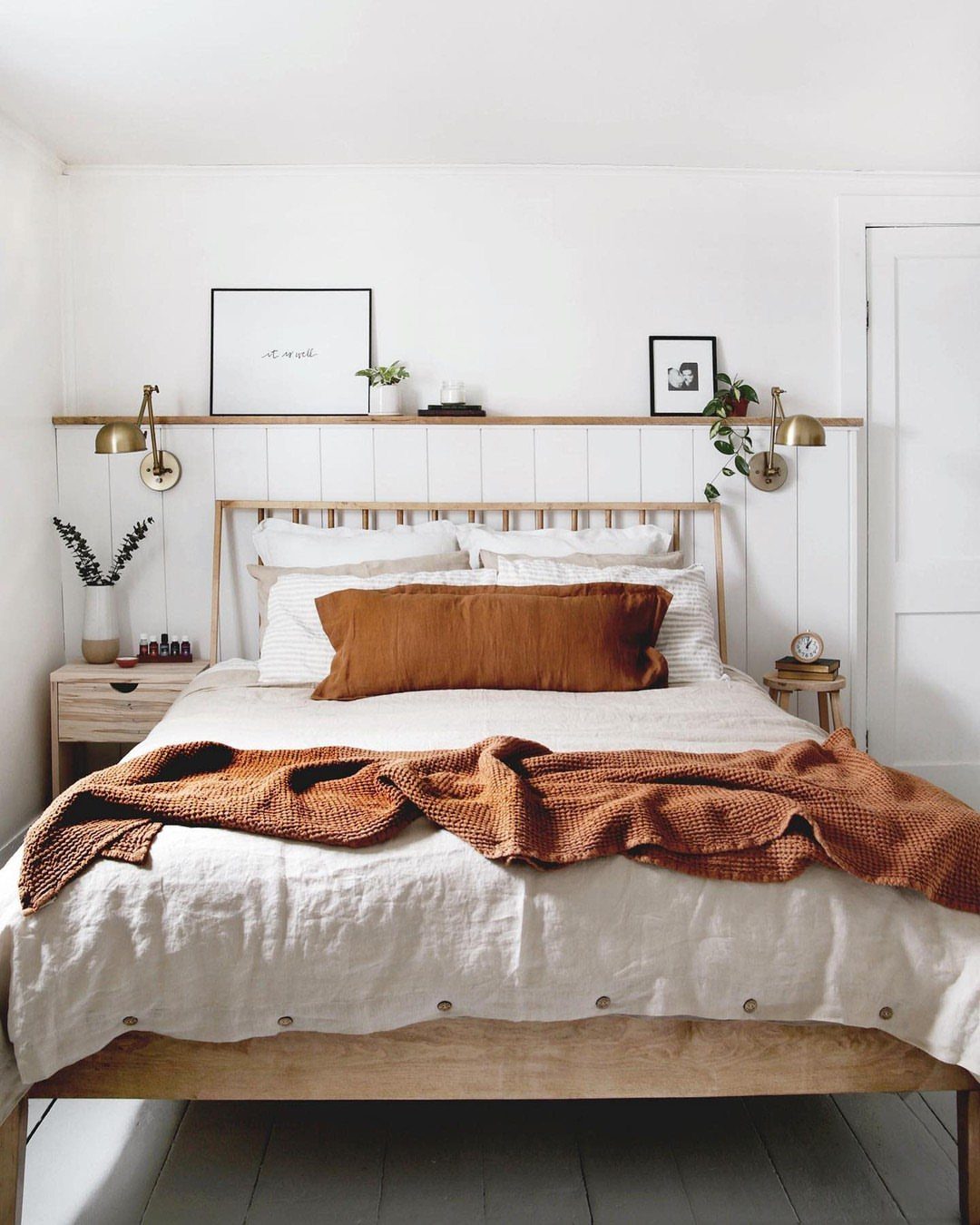Wooden bed with white linens and a decorative ledge with art above it.
