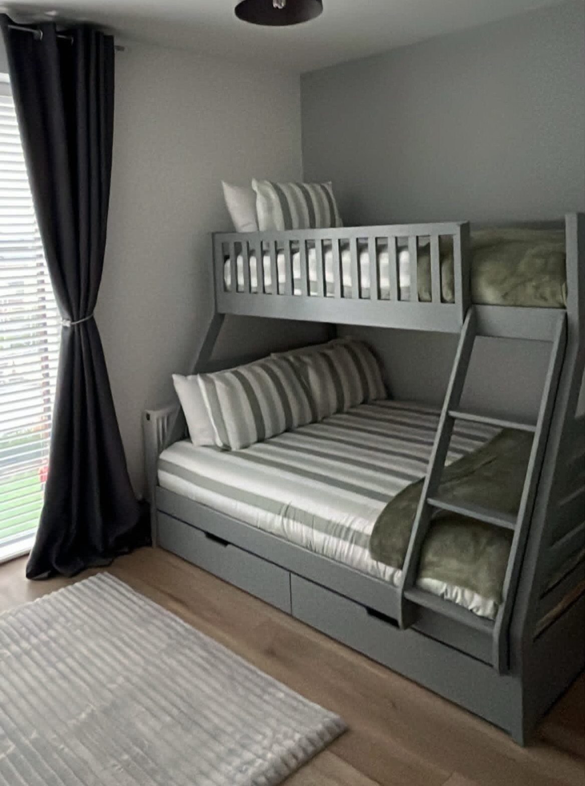 Grey wooden bunk bed with striped bedding and storage drawers underneath in a bedroom.