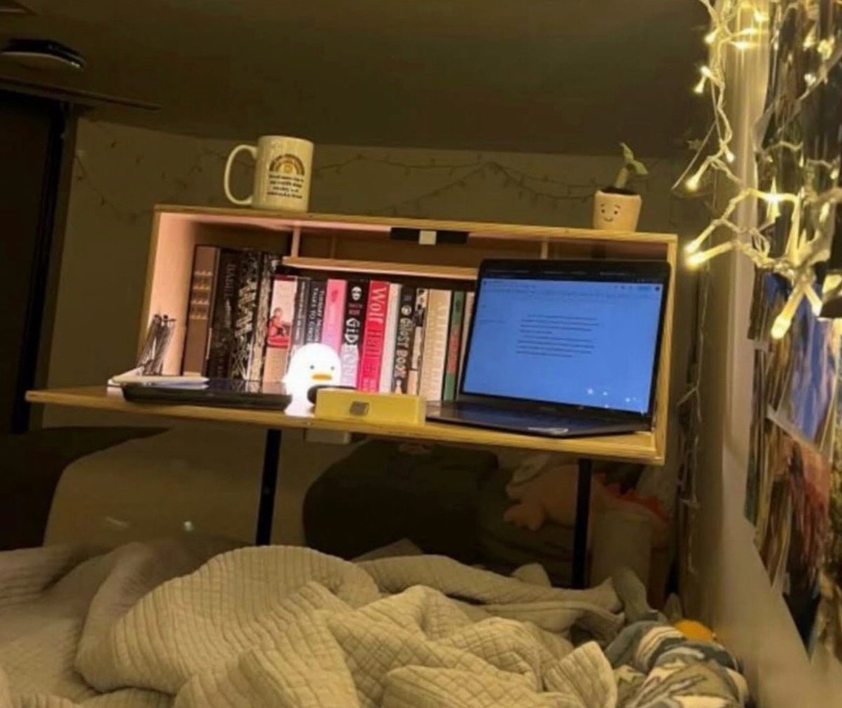 Small wooden workstation desk attached to a bed with a laptop and books.