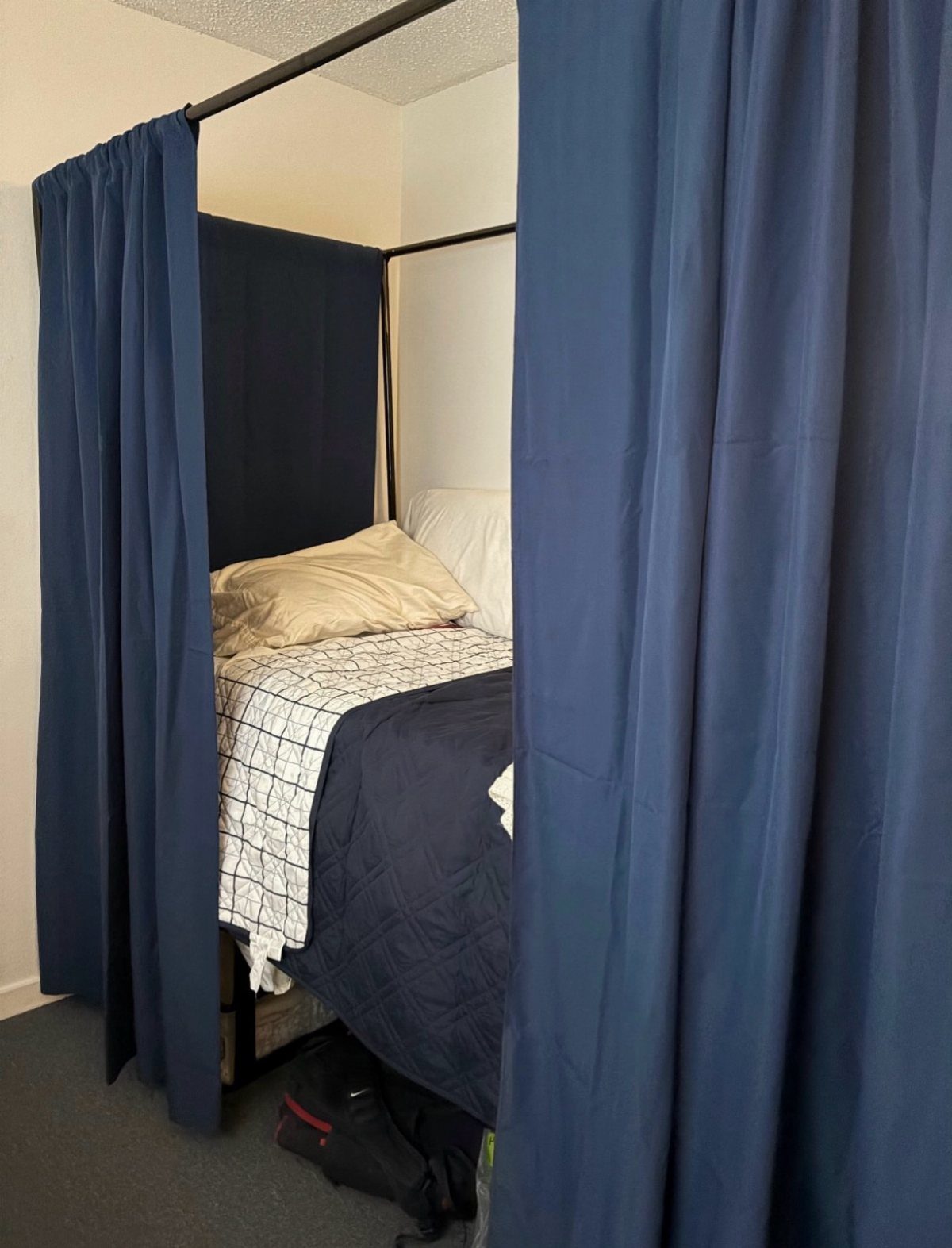 Navy blue curtains surrounding a bed with a white and blue comforter.